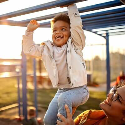 A young boy on the autism difference is playing on the monkey bars with his mother's help to work with his Movement Differences