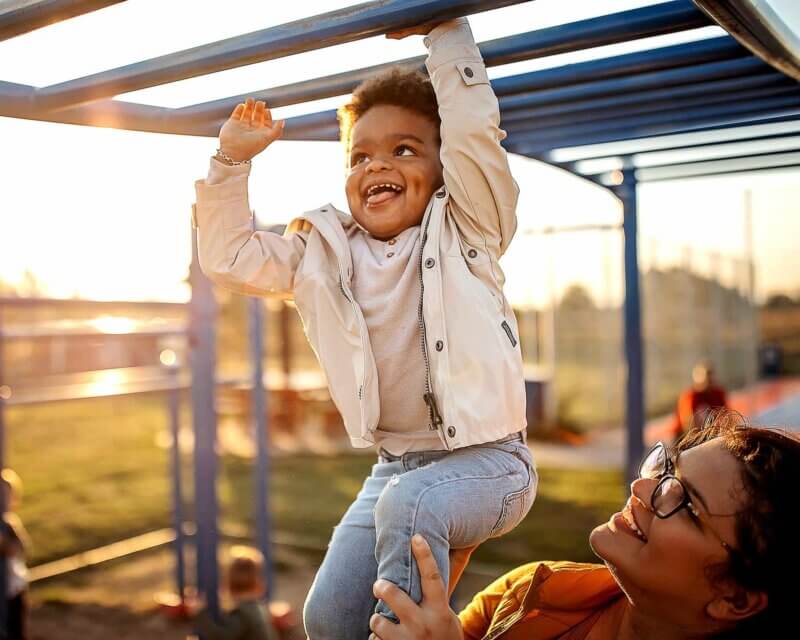 A young boy on the autism difference is playing on the monkey bars with his mother's help to work with his Movement Differences