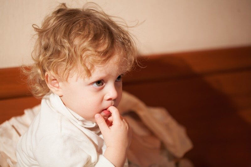 Adorable thoughtful little child with curly blond hair sitting chewing a finger and staring ahead... child with autism stimming while chewing a finger