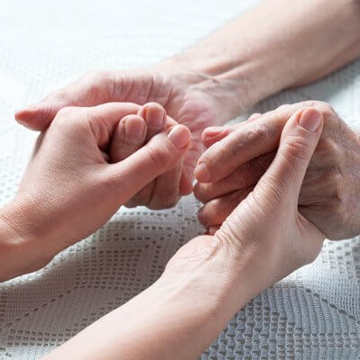 Aging caregiver holds hand of young person with disabillity