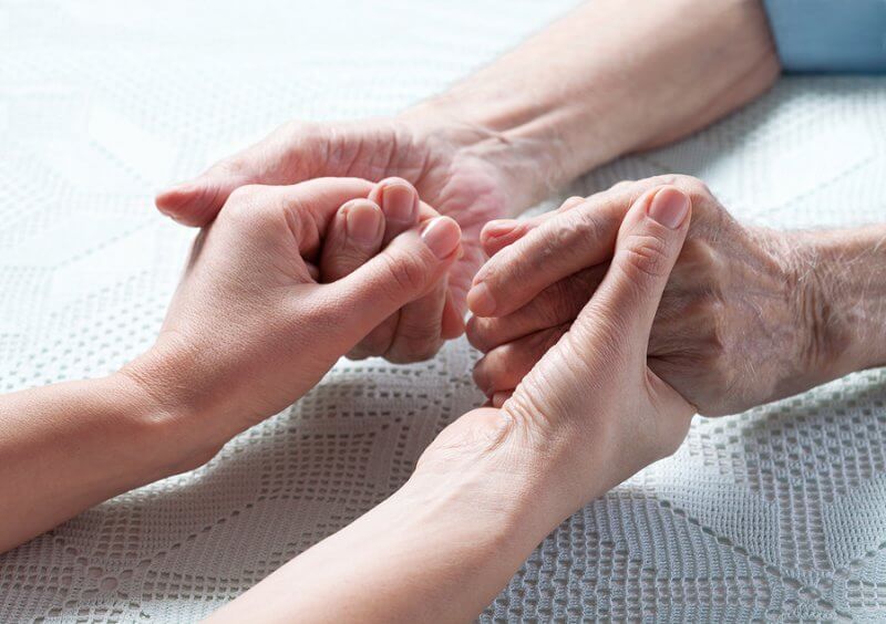 Aging caregiver holds hand of young person with disabillity