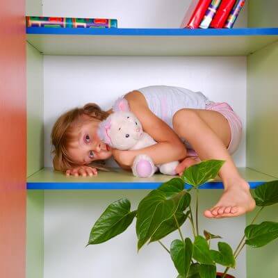 little girl with autism and unusual fears lying on a bookshelf with her toy cat