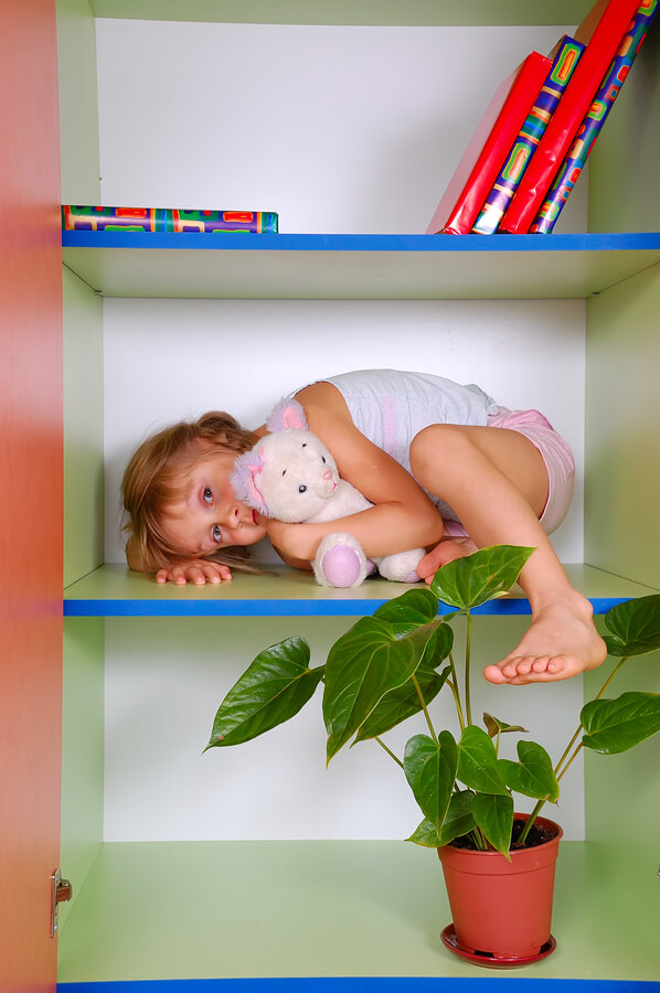 little girl with autism and unusual fears lying on a bookshelf with her toy cat