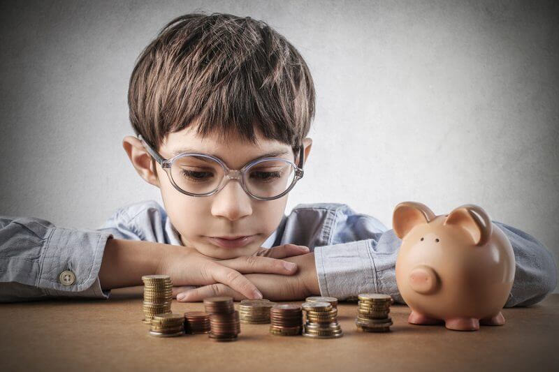 money managment for boy with autism looking at piles of money with his piggy bank