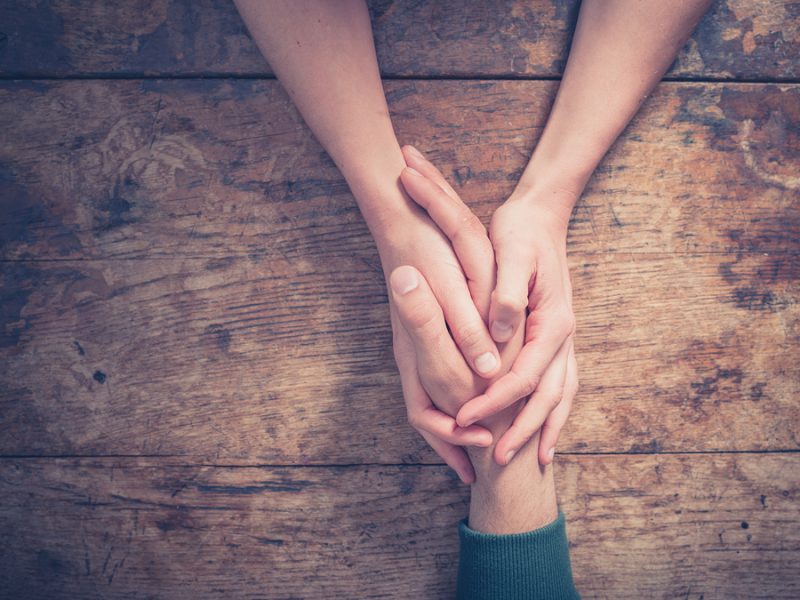 Keeping marriage strong with autism diagnosis: Close up on a man and a woman holding hands at a wooden table