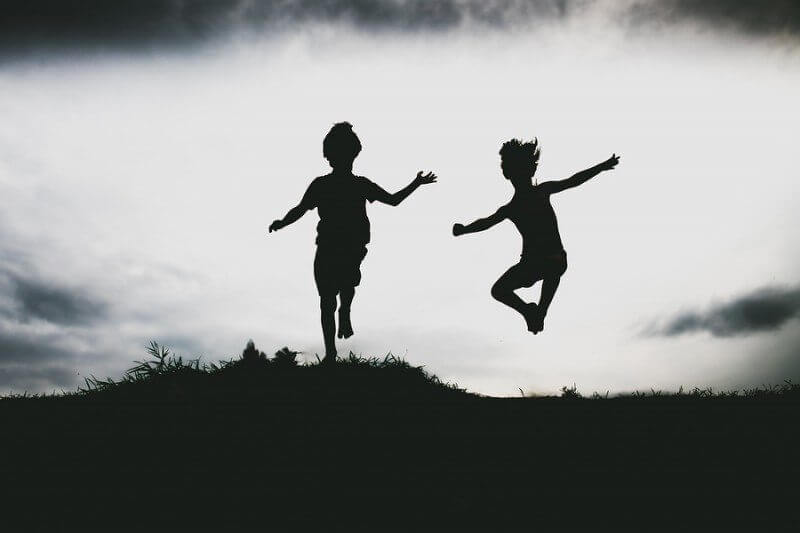 Silhouettes of siblings with autism jumping from a sand cliff at the beach.