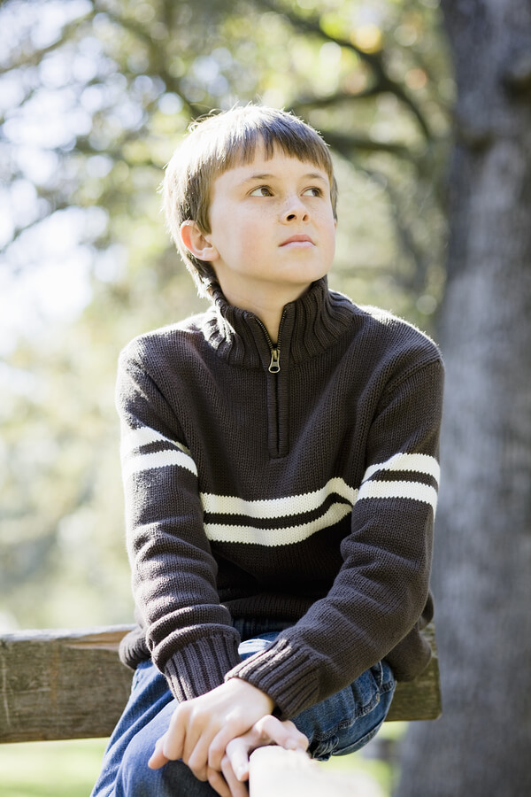 Portrait of a Cute Young Boy Sitting on a Wooden Railing Looking Away From Camera. eye contact with autism