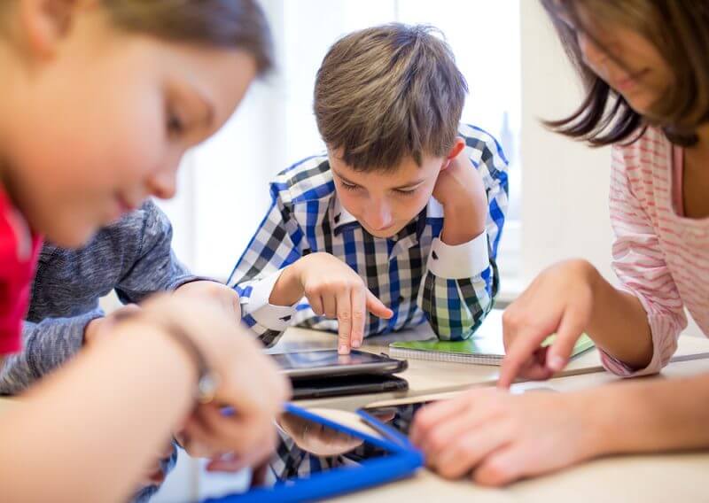 education, elementary school, learning, technology and people concept - group of school kids with tablet pc computer having fun on break in classroom. Autism technology and apps